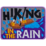 The words Hiking In The Rain surround two brown shoes walking up a hill in the rain.