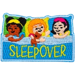 Three little girls are pretending to be asleep in bed. The word Sleepover is across the blanket.
