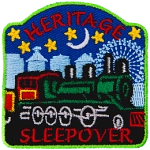 A green train is in the center of the patch, with blue buildings behind it and the night sky. The words Heritage Sleepover are stitched above and below.