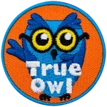This blue, glasses-wearing owl has their right wing over their heart and their left raised in the air. The words True Owl are embroidered at the bottom of this round patch.