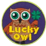 A brown owl with big green eyes holds a four-leaf clover in his wing. The words Lucky Owl is written in yellow near the bottom of the patch.