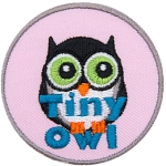 A small black owl with a white belly stares off into the distance. The words Tiny Owl are written in blue text near the bottom of the patch.