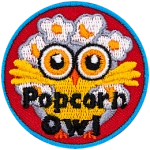 A yellow owl with big orange eyes has its wings spread open wide. Popped popcorn kernels cover the owl's hair.