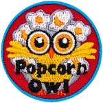 A yellow owl with big orange eyes has its wings spread open wide. Popped popcorn kernels cover the owl's hair.