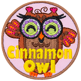 A brown owl with purple glasses with green lenses. The words Cinnamon Owl are stitched across the bottom.