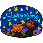 A boy and a girl stand on a grassy hill and look up at the starry sky. The text Stargazing is embroidered amongst the stars.