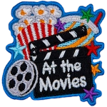 A clapperboard with the words At The Movie rests against a popcorn bucket. A roll of film is next to it.
