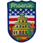 The word Phoenix is above a tiered building in a desert. The flag of the USA is in the background.