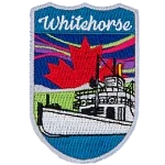 Whitehorse is stitched above a white river boat. There is a red maple leaf in the sky with the northern lights.