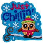 A little owl is bundled up in a toque and scarf as it sits on a snow-covered tree branch. The text Just Chillin' sits above it.