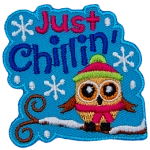 A little owl is bundled up in a toque and scarf as it sits on a snow-covered tree branch. The text Just Chillin' sits above it.