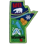This crest is shaped like the province of Manitoba. Decorating it are the initials MB, a polar bear, the aurora Borealis, a snowflake, two loonie coins, a lake, a pair of slippers, and the capital Winnipeg.