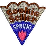 The words Cookie Seller Spring are on a cookie slice with blue icing and a pink flower.