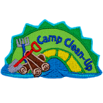 A green and yellow sea serpent with the words Camp Clean-Up on it and a pile of wood, a shove and a rake next to it.