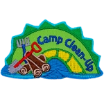 A green and yellow sea serpent with the words Camp Clean-Up on it and a pile of wood, a shove and a rake next to it.